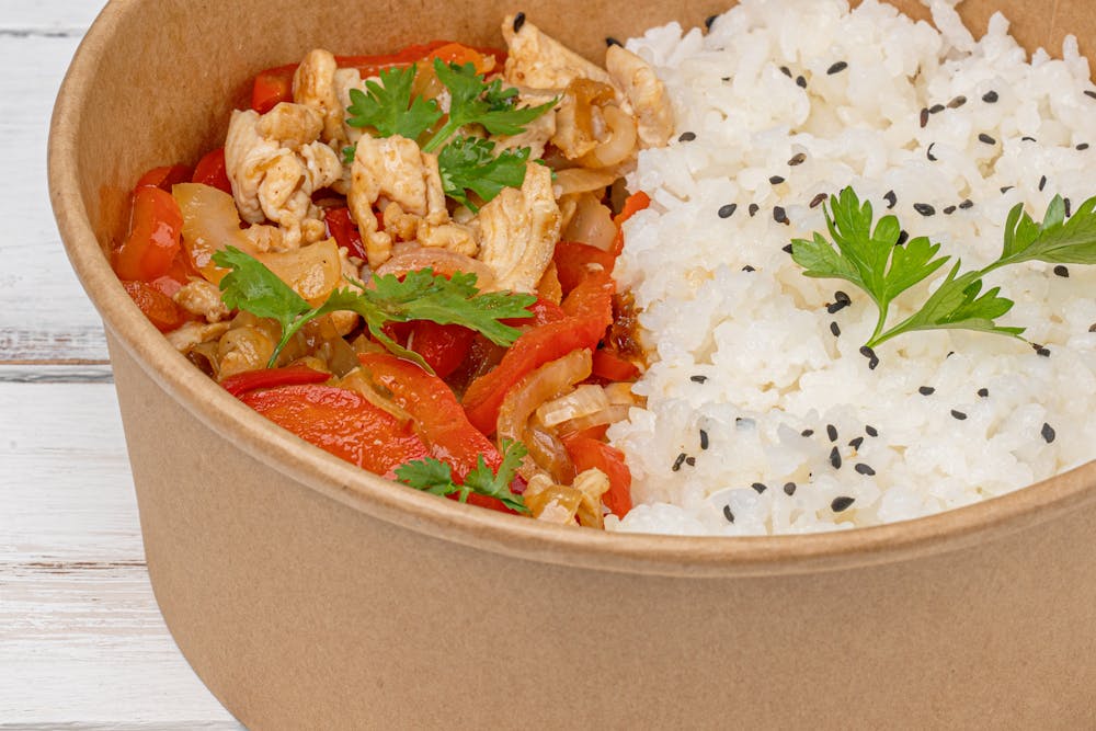 A kraft bowl filled with rice, vegetables and herbs