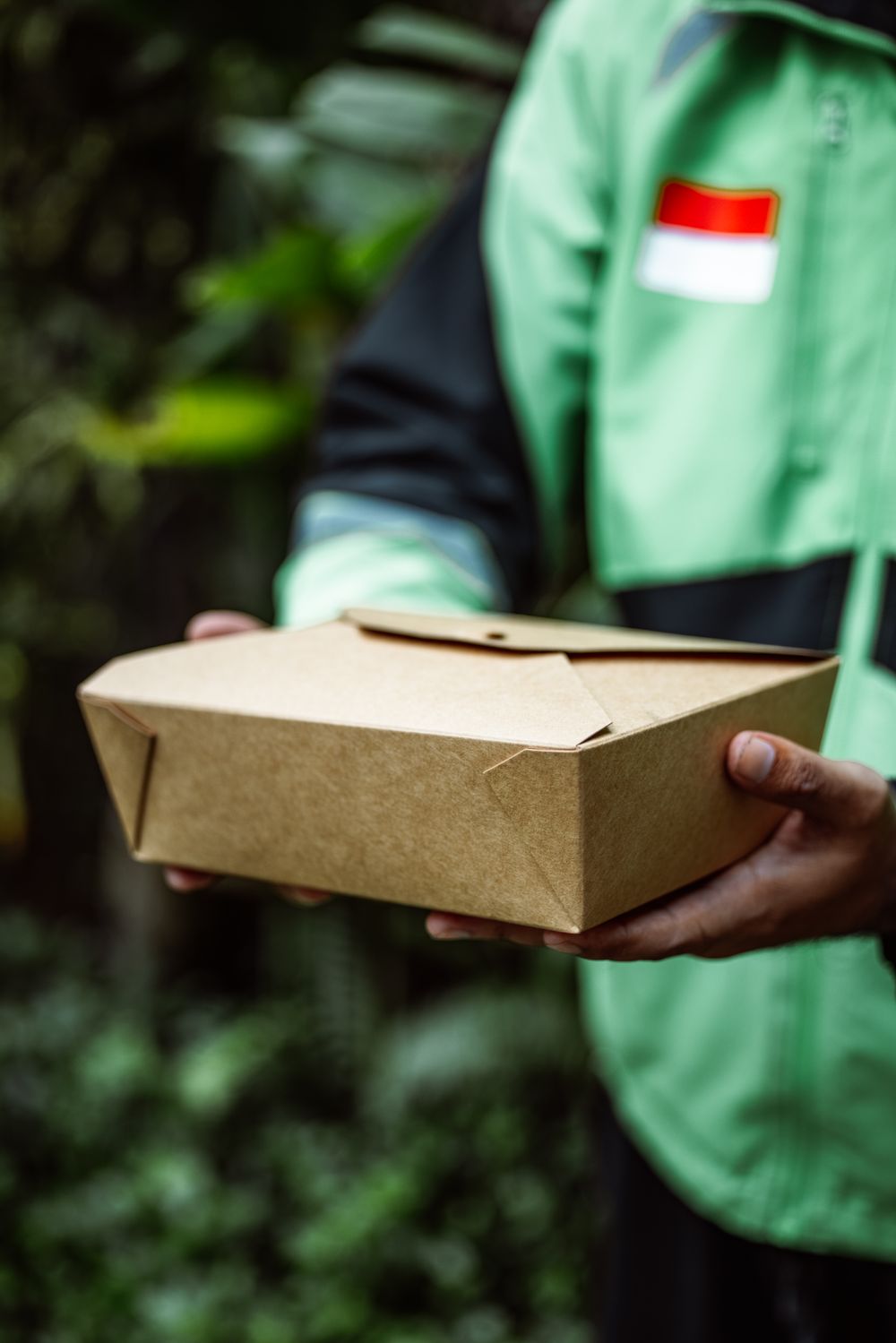 A person holding a kraft takeaway box outdoors