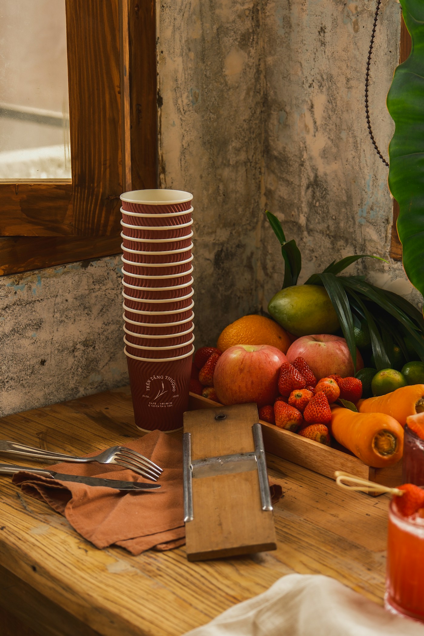 A stack of kraft cups beside a tray of fresh fruit on a wooden table